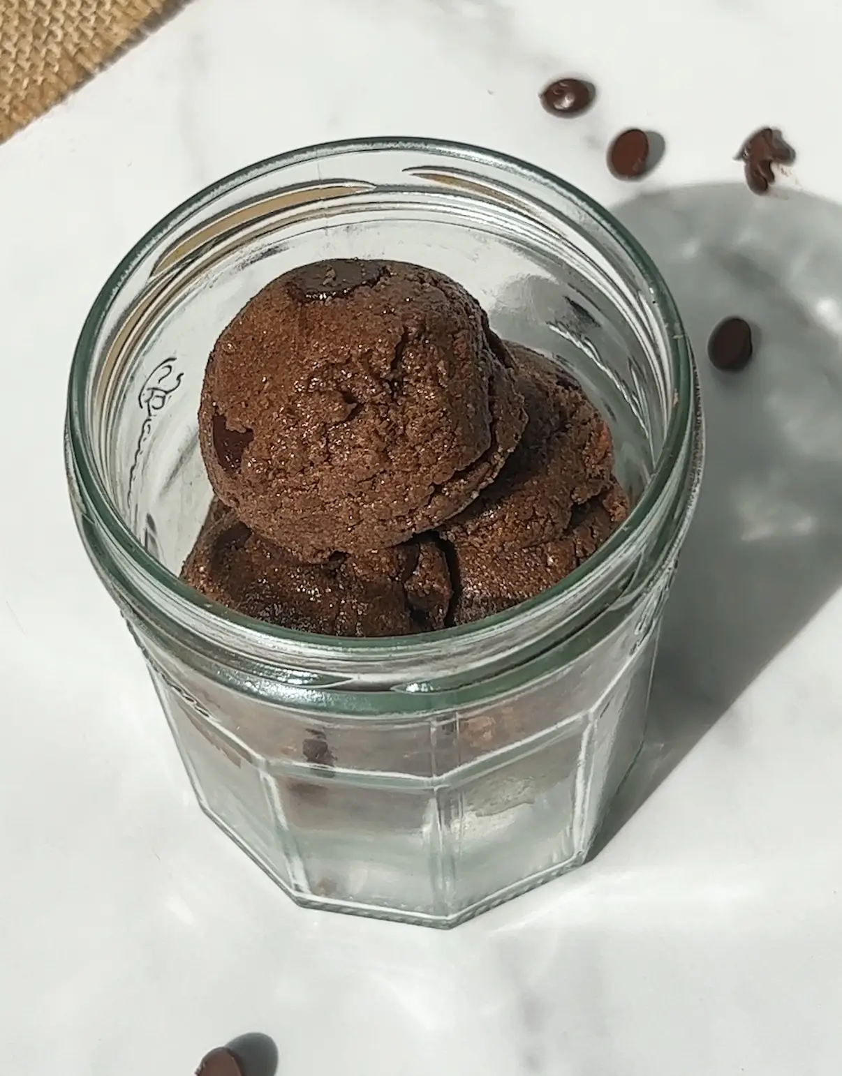 Scoops of edible protein brownie batter studded with chocolate chips in a glass jar
