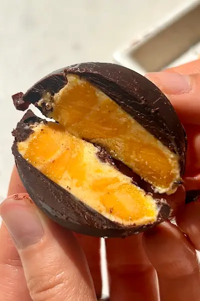 No-bake mango yogurt chocolate bites stacked showing dark chocolate shell with mango yogurt filling