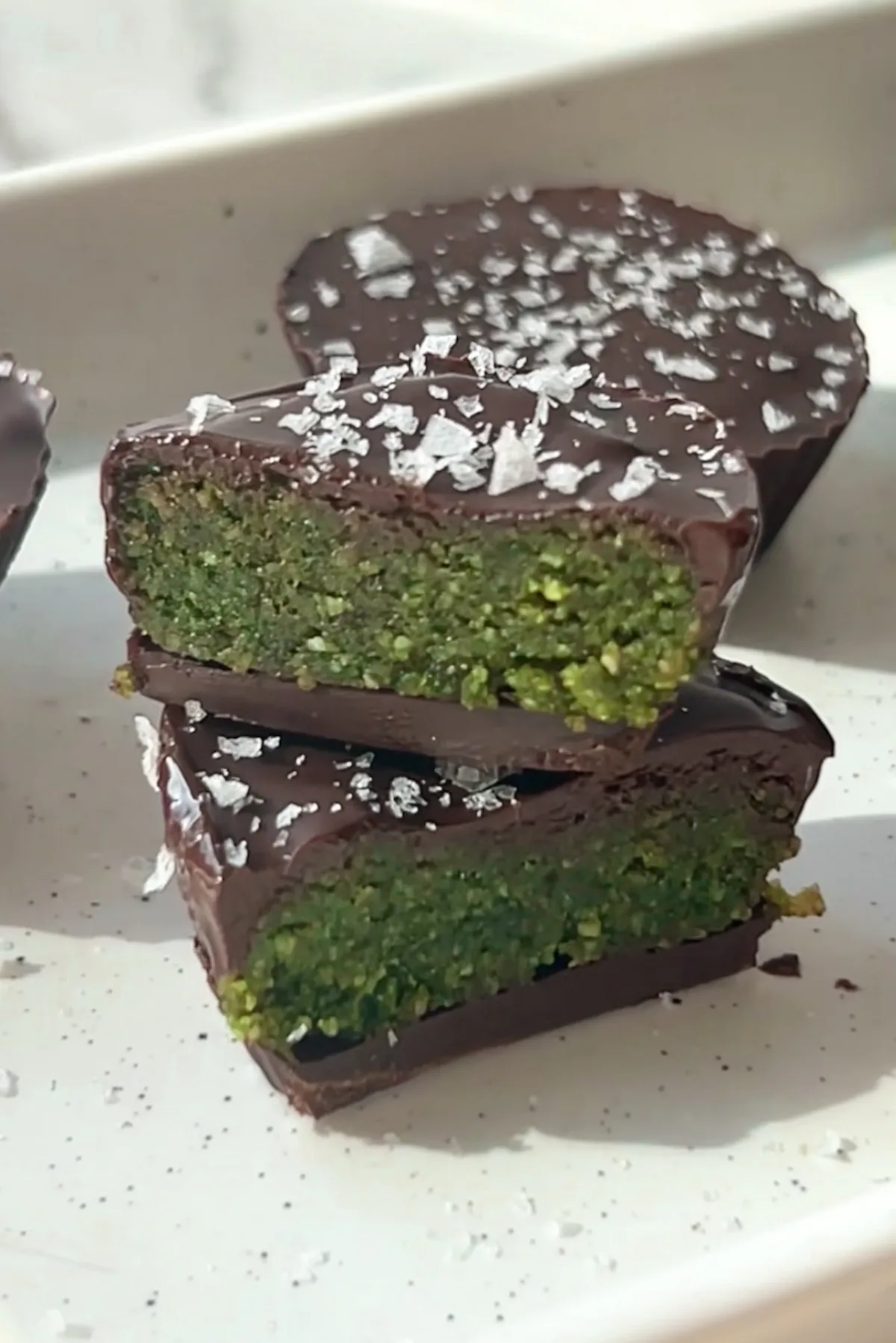 Hand holding a no bake matcha chocolate cup broken in half revealing a soft green matcha almond flour filling inside a dark chocolate shell