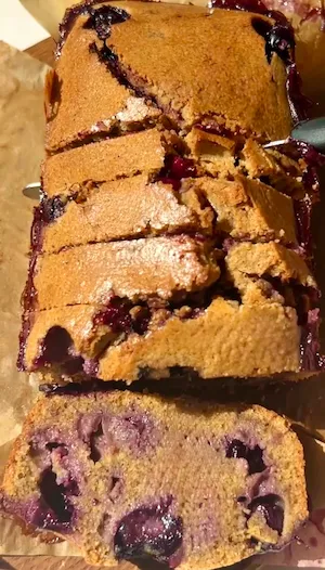 A hand holding a slice of mini blueberry olive oil loaf cake showing the golden crumb with juicy blueberries