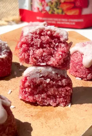 no bake strawberry coconut bites coated in pink coconut with a pale pink icing drizzle