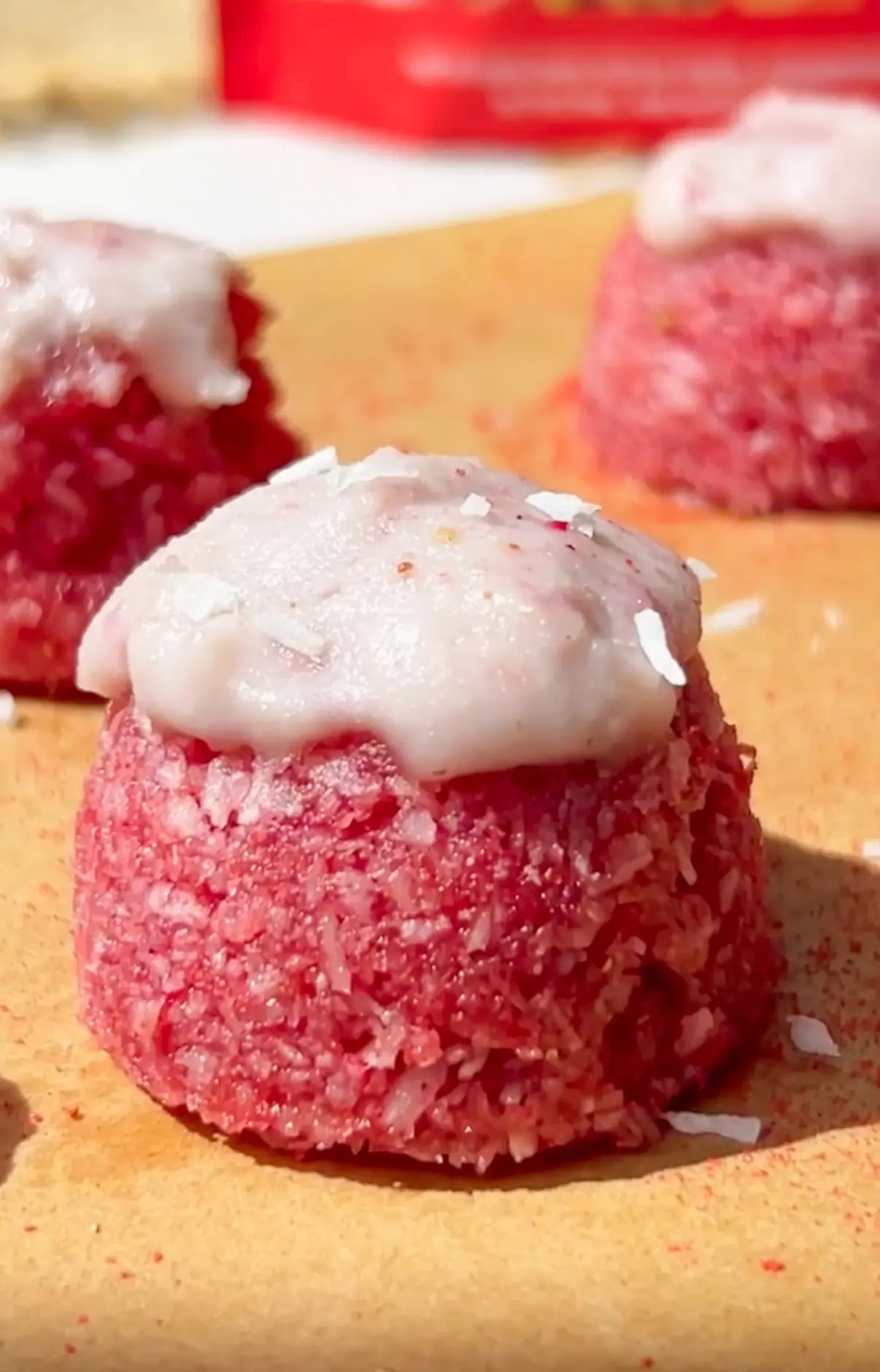 no bake strawberry coconut bites coated in pink coconut and topped with a pale pink icing drizzle and coconut flakes